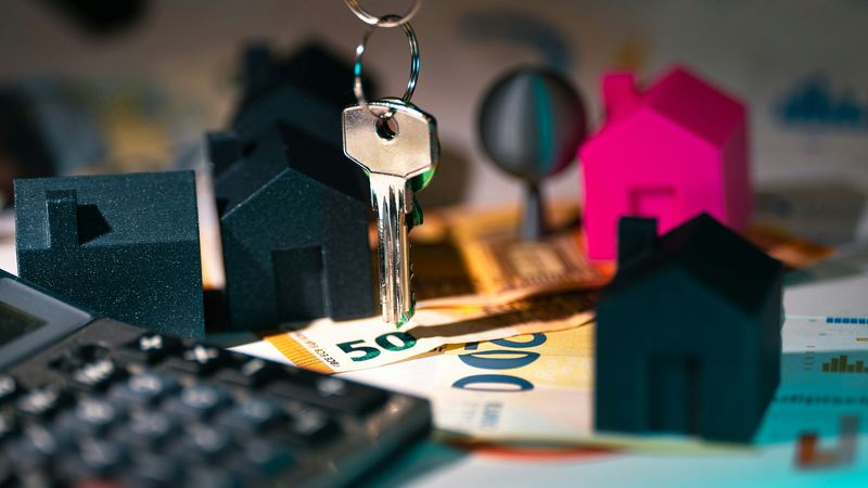 A calculator, house keys and a small model house on a desk