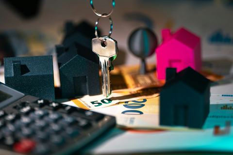 A calculator, house keys and a small model house on a desk